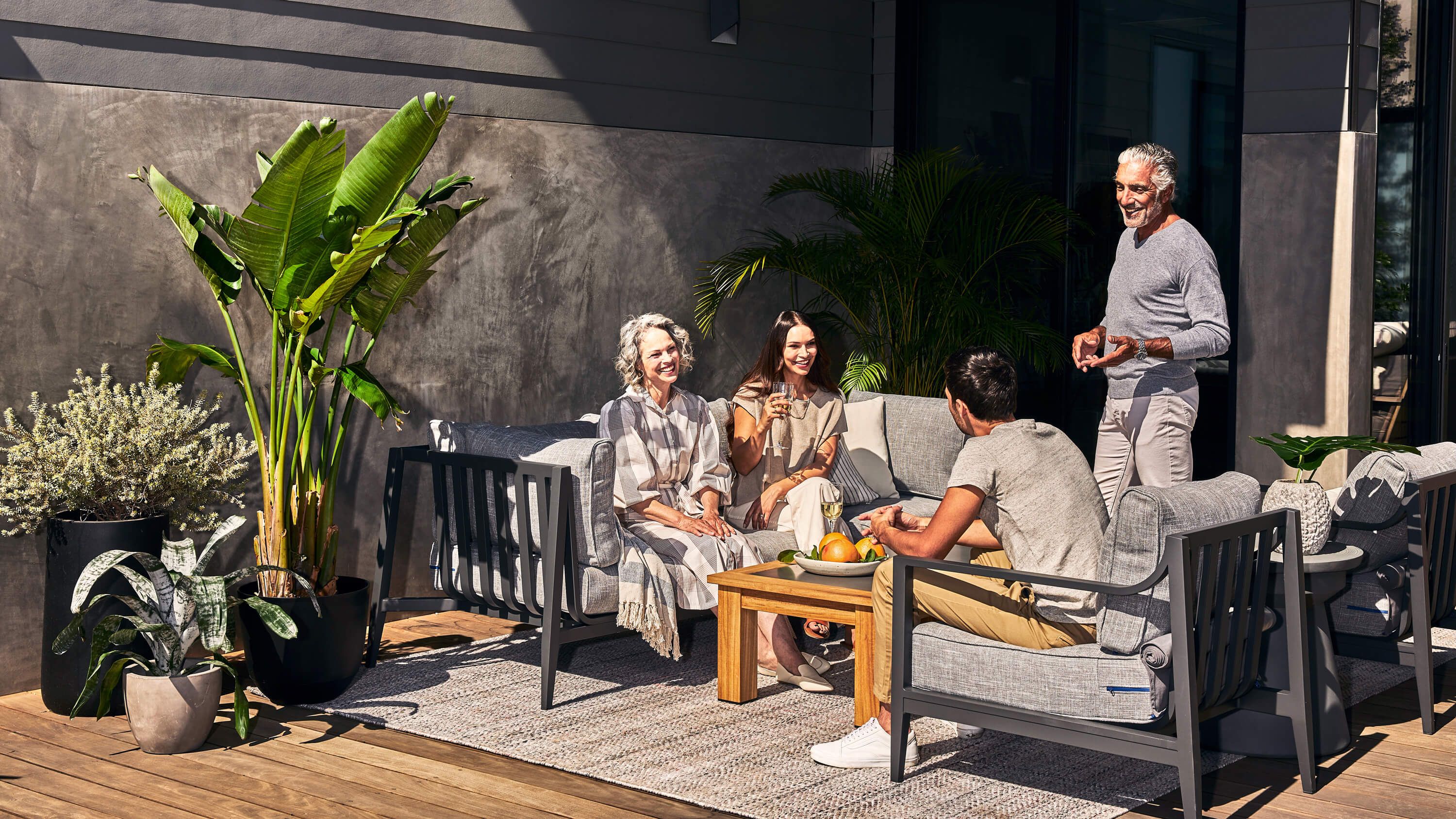 The charcoal aluminum 5 piece sofa with armchairs being enjoyed by a family outdoors.