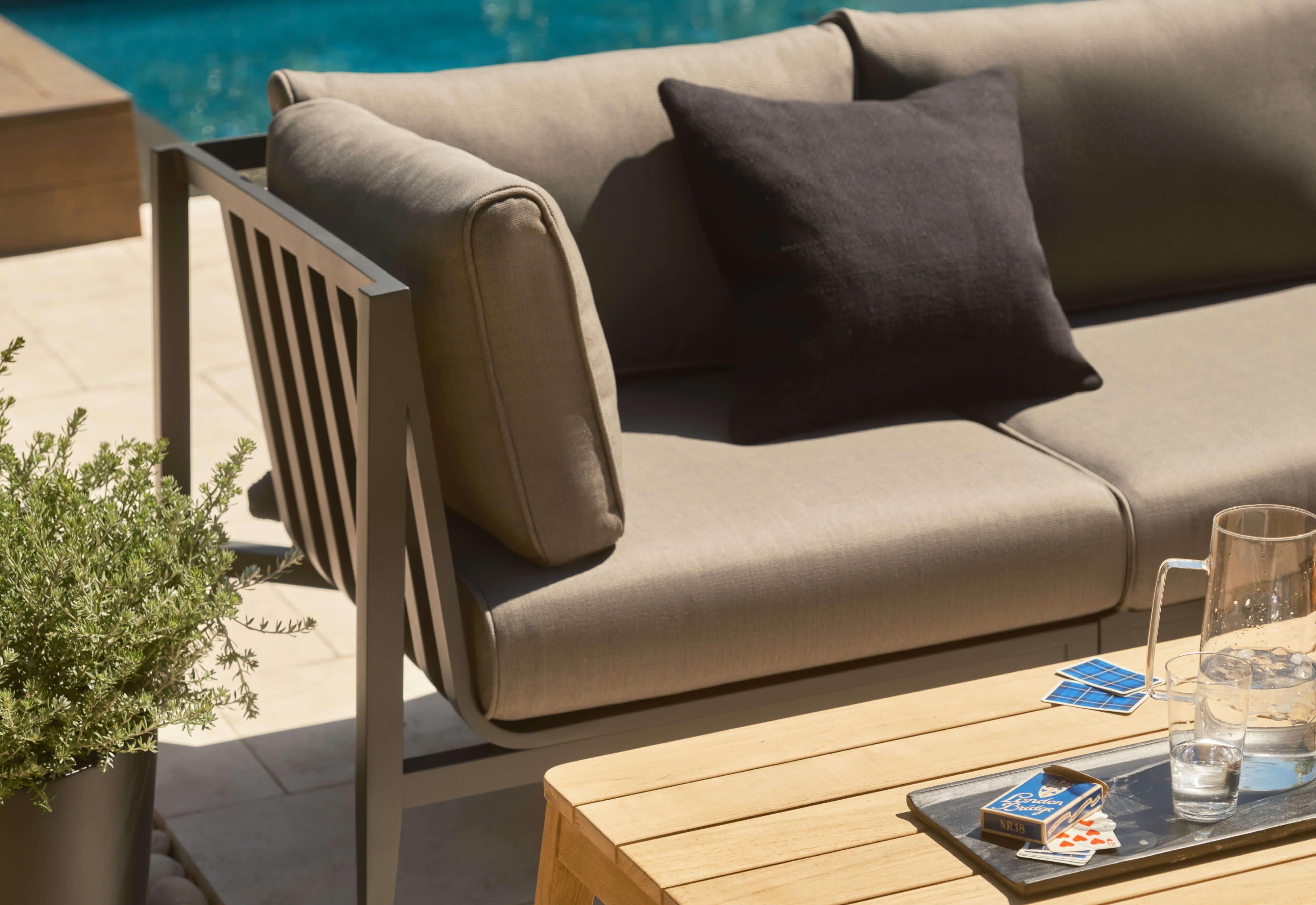 Closeup of the charcoal aluminum sofa with dark pebble gray cushions and the tapered leg teak coffee table.
