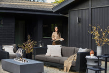 The black wicker outdoor sofa and armchair in dark pebble gray shown in a backyard on a gravel surface.