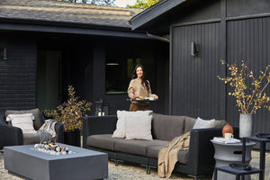 The black wicker outdoor sofa and armchair in dark pebble gray shown in a backyard on a gravel surface.