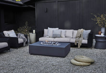 Black wicker with sandstone gray cushions in a 3 seat sofa and armchairs featured on a gravel substrate.