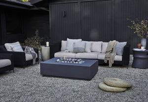 Black wicker with sandstone gray cushions in a 3 seat sofa and armchairs featured on a gravel substrate.