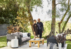 The black wicker loveseat and armchairs with sandstone cushions in a green backyard setting.